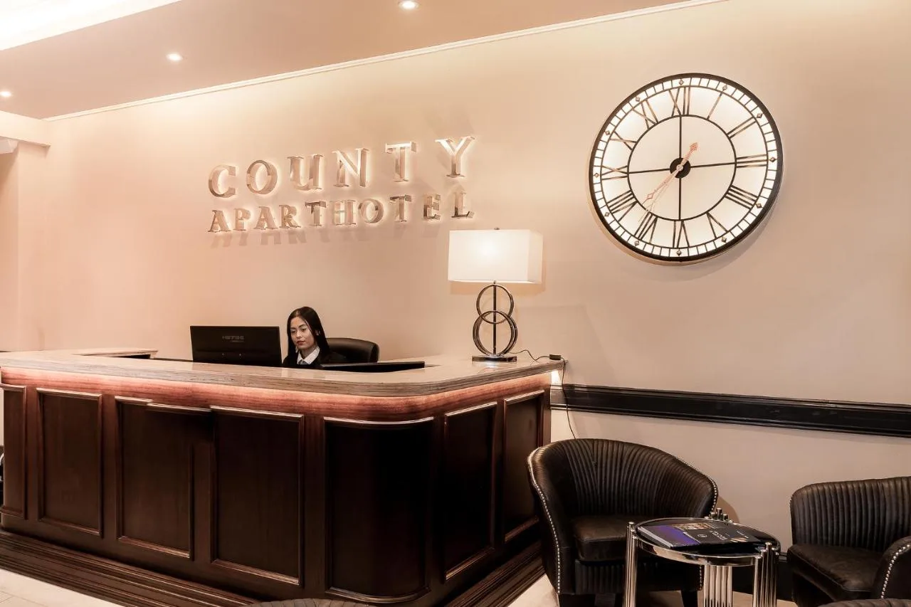 a woman sitting at a counter with a clock on the wall at The County Aparthotel in Newcastle upon Tyne